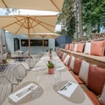 Grande terrasse en bois ombragée avec parasols et banquette en lisière de forêt à Maison B Bridel.
